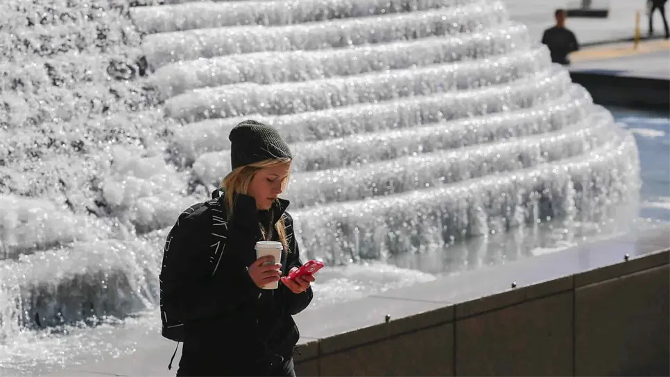 Una mujer observando su celular frente a una fuente congelada en el parque de Woodruff, en el centro de Atlanta, Georgia (EEUU). EFE/Erik S. Lesser