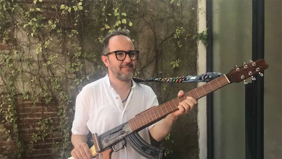 El artista colombiano César López posa con una guitarra en forma de rifle AK-47. FOTO: Cortesía.